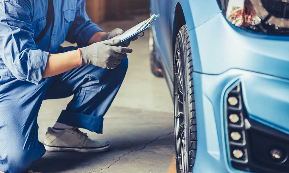 car mechanic technician holding clipboard and checking the maintenance on a vehicle