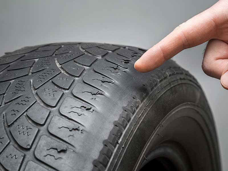 finger pointing to the old, damaged and worn black tire tread